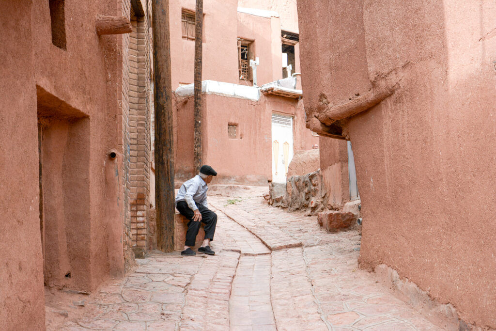 lone figure quiet alley ancient pink red mud brick walls Abyaneh Iran fine art street photography by Hadi Baradaran ArtQuestor