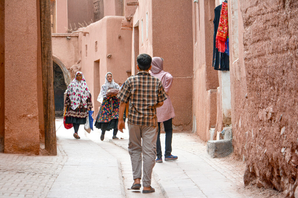 people walking narrow alley Abyaneh Iran traditional shops mud brick walls fine art street photography by Hadi Baradaran ArtQuestor